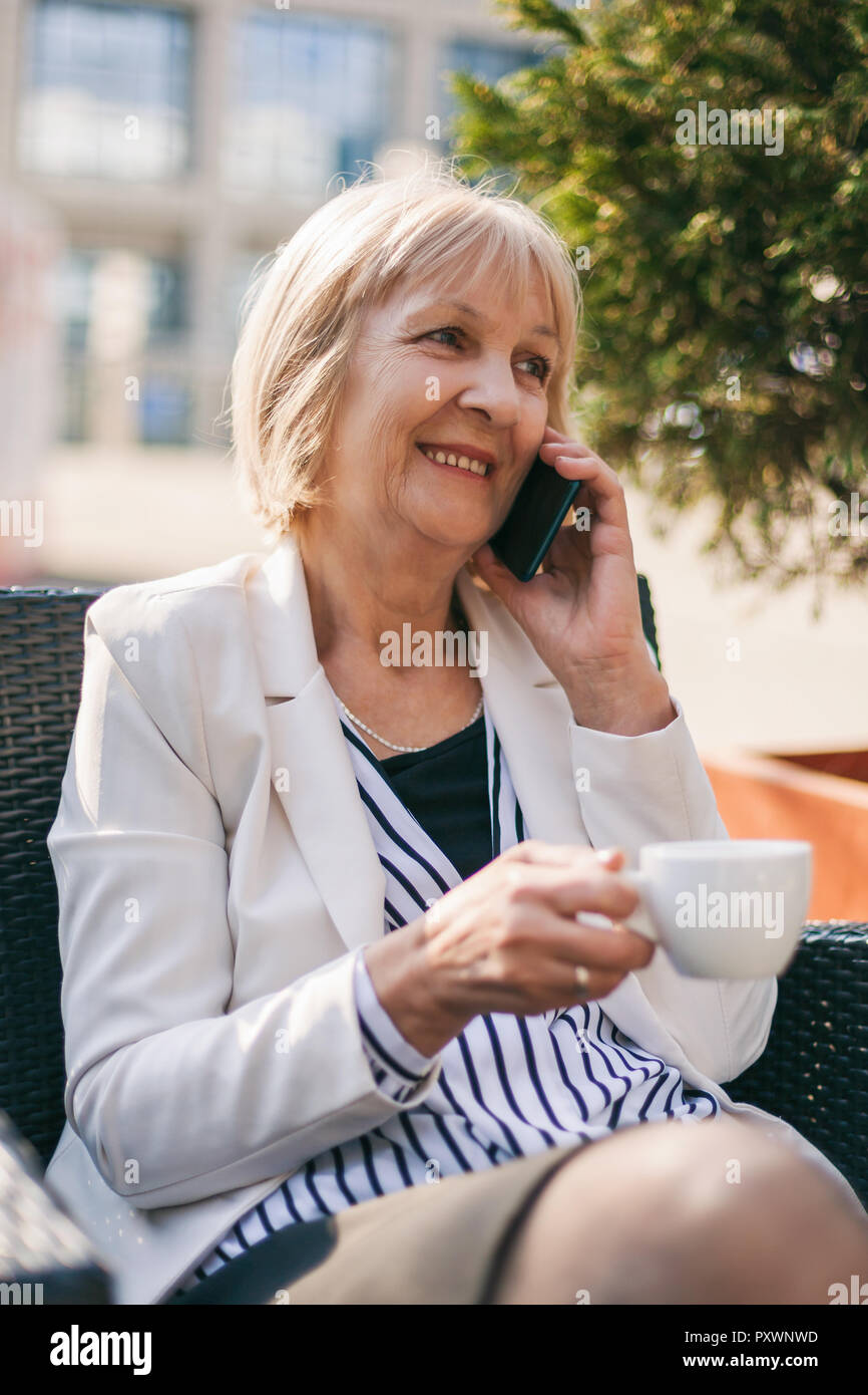 Senior imprenditrice è seduta in cafe e parlando al telefono. Foto Stock