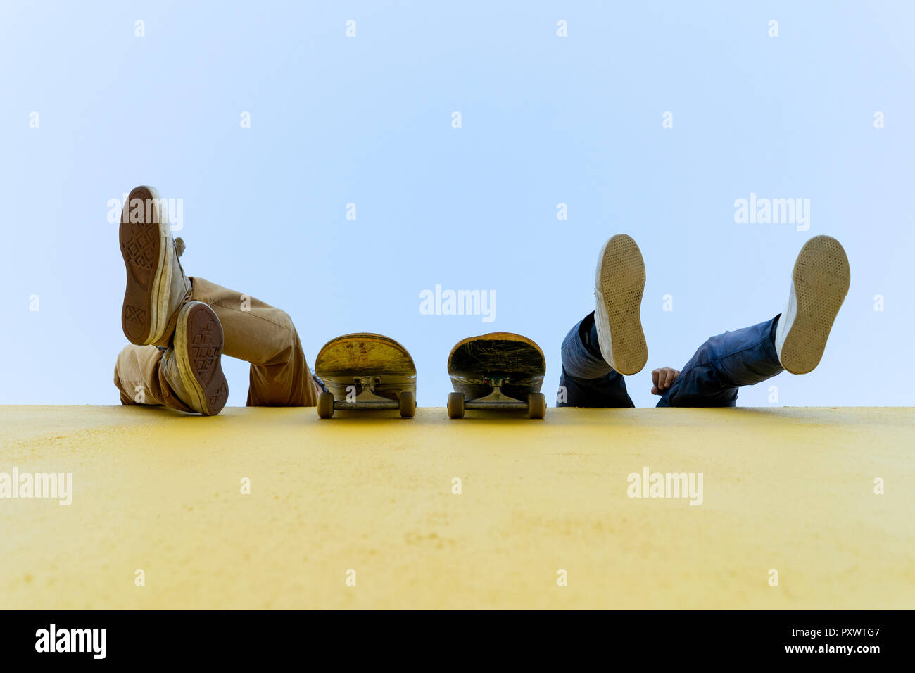 Gambe di due uomini con skateboard seduto su un alto muro giallo Foto Stock