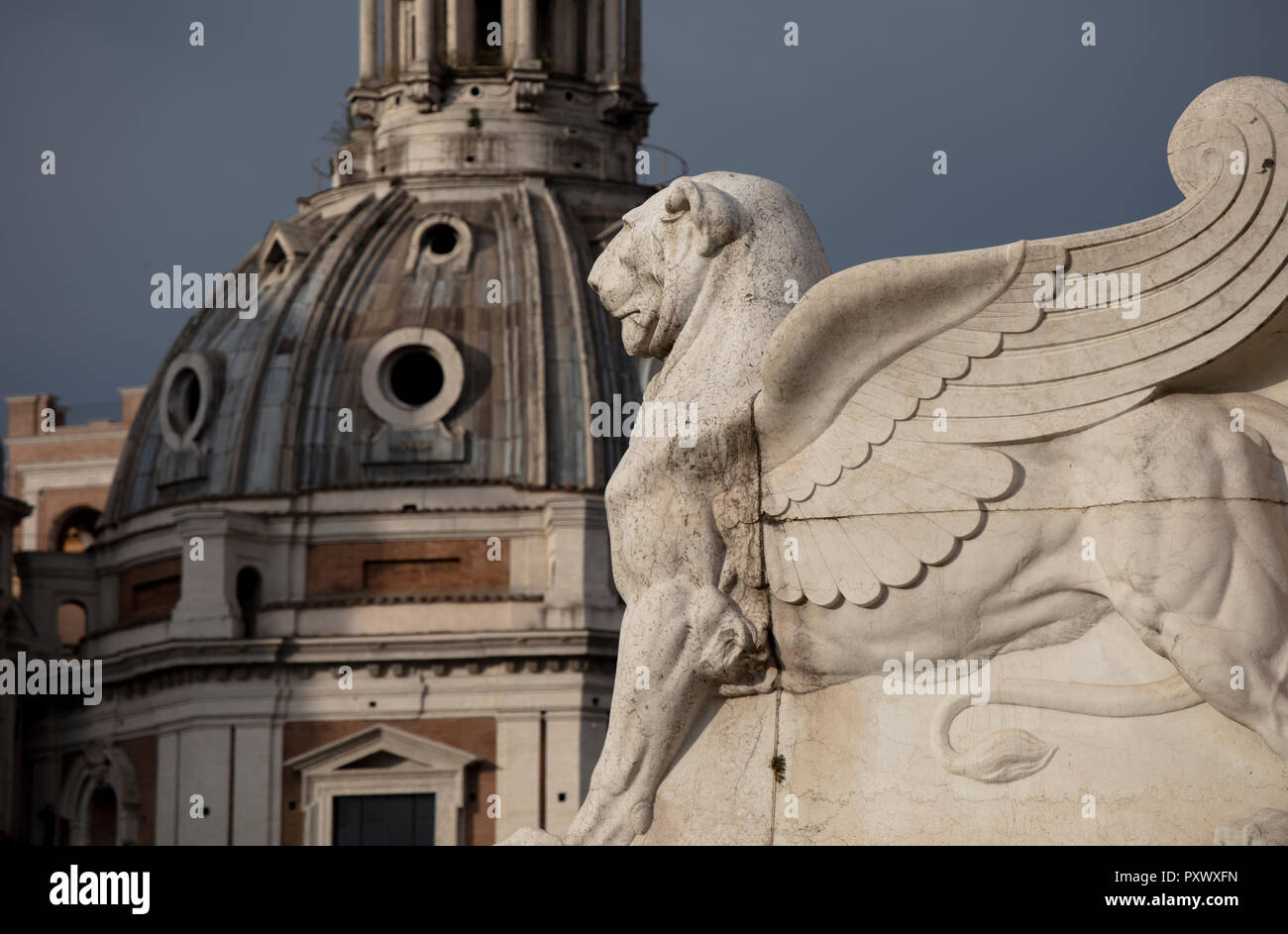 Un leone alato statua alla base dell'Altare della Patria in piazza Venezia a Roma. In fondo è la cupola barocca di Santa Maria di Loreto. Foto Stock