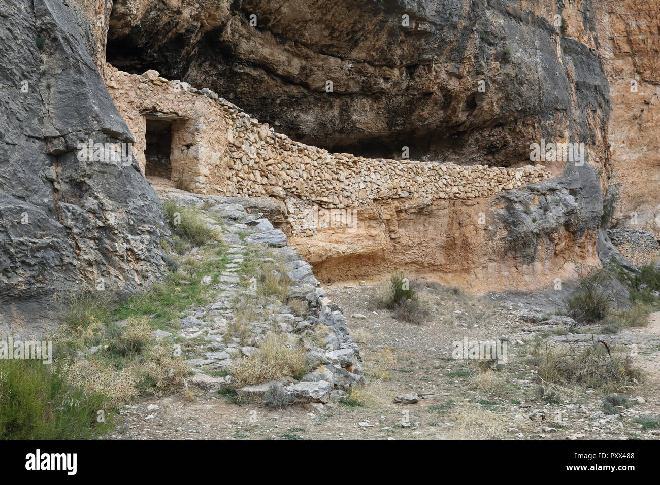 Un rifugio di pastori e bestiame in pietra del muro a secco all'interno di una grotta nella Red Rock ferroso del Barranco de la Hoz Seca canyon, Jaraba, Spagna Foto Stock