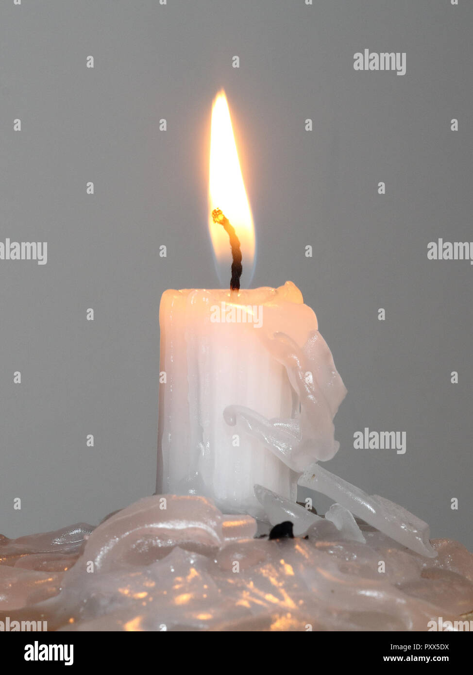 Una candela accesa con un giallo fiamma ardente e fusione di gocce di cera su un luminoso ruvida la superficie di legno e uno sfondo bianco Foto Stock