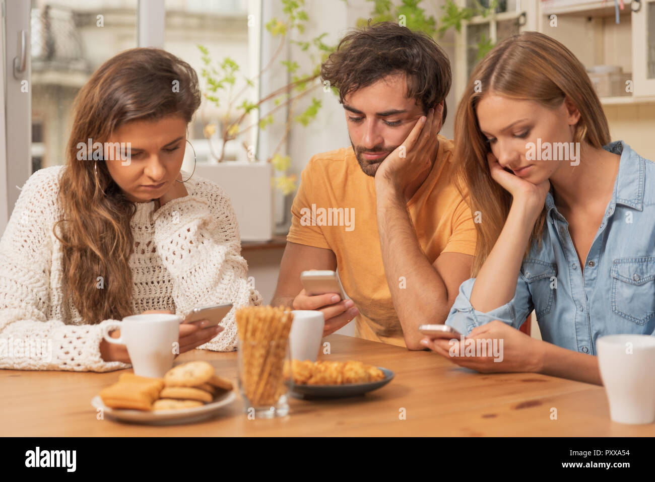 Amici seduti in cucina e guardare sui loro telefoni. La navigazione in Internet e la tecnologia concetto di dipendenza Foto Stock