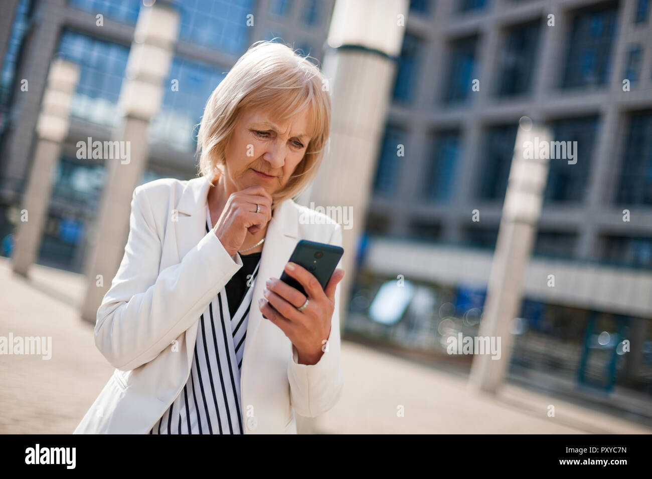 Outdoor ritratto di preoccupato senior imprenditrice che sta utilizzando lo smartphone. Foto Stock
