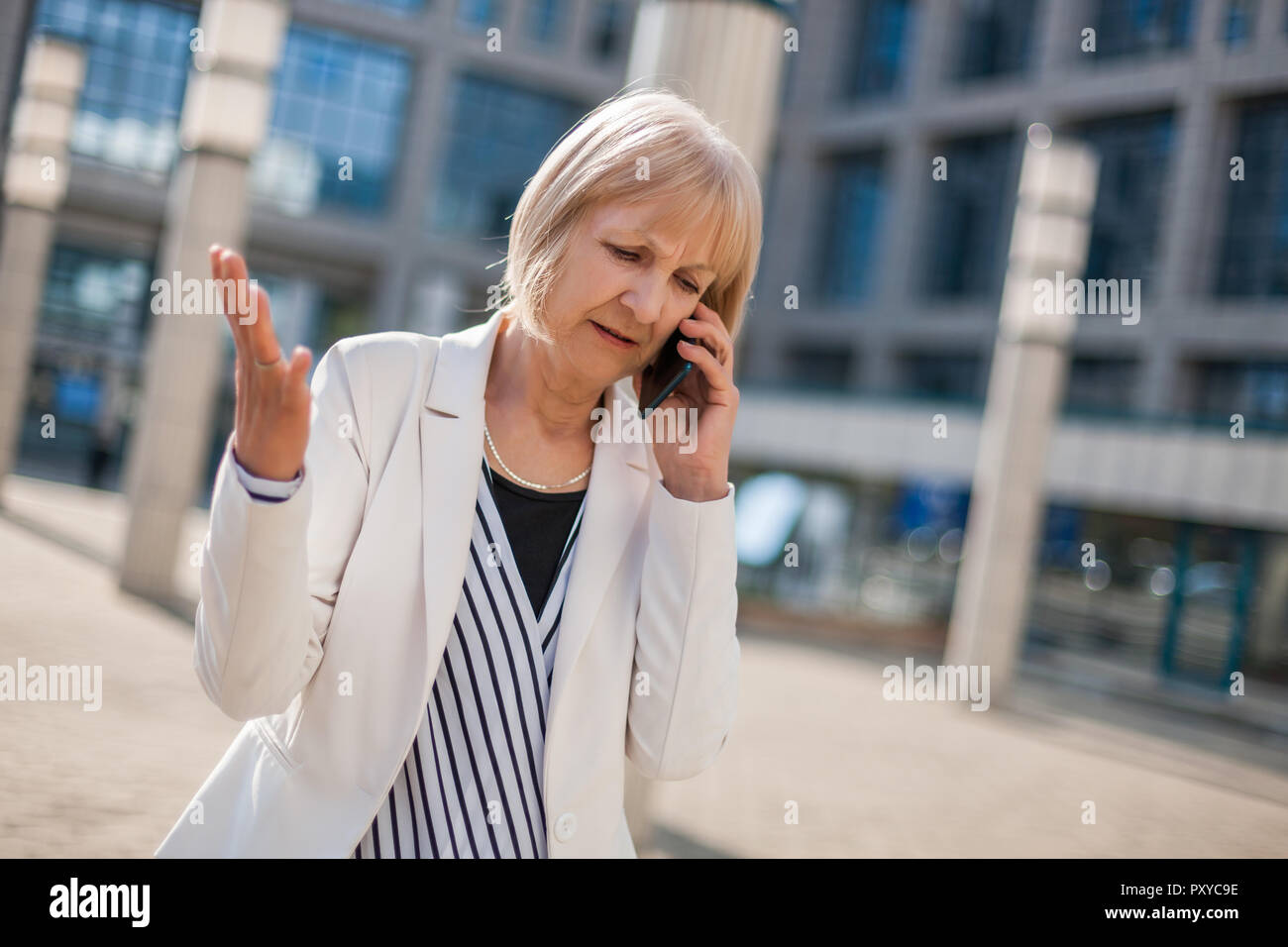 Outdoor ritratto di angry senior imprenditrice che sta parlando al telefono. Foto Stock