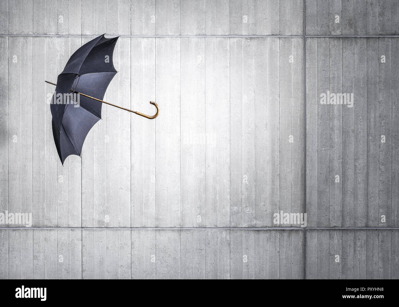 Schwarzer Regenschirm fliegt Betonwand vor Foto Stock
