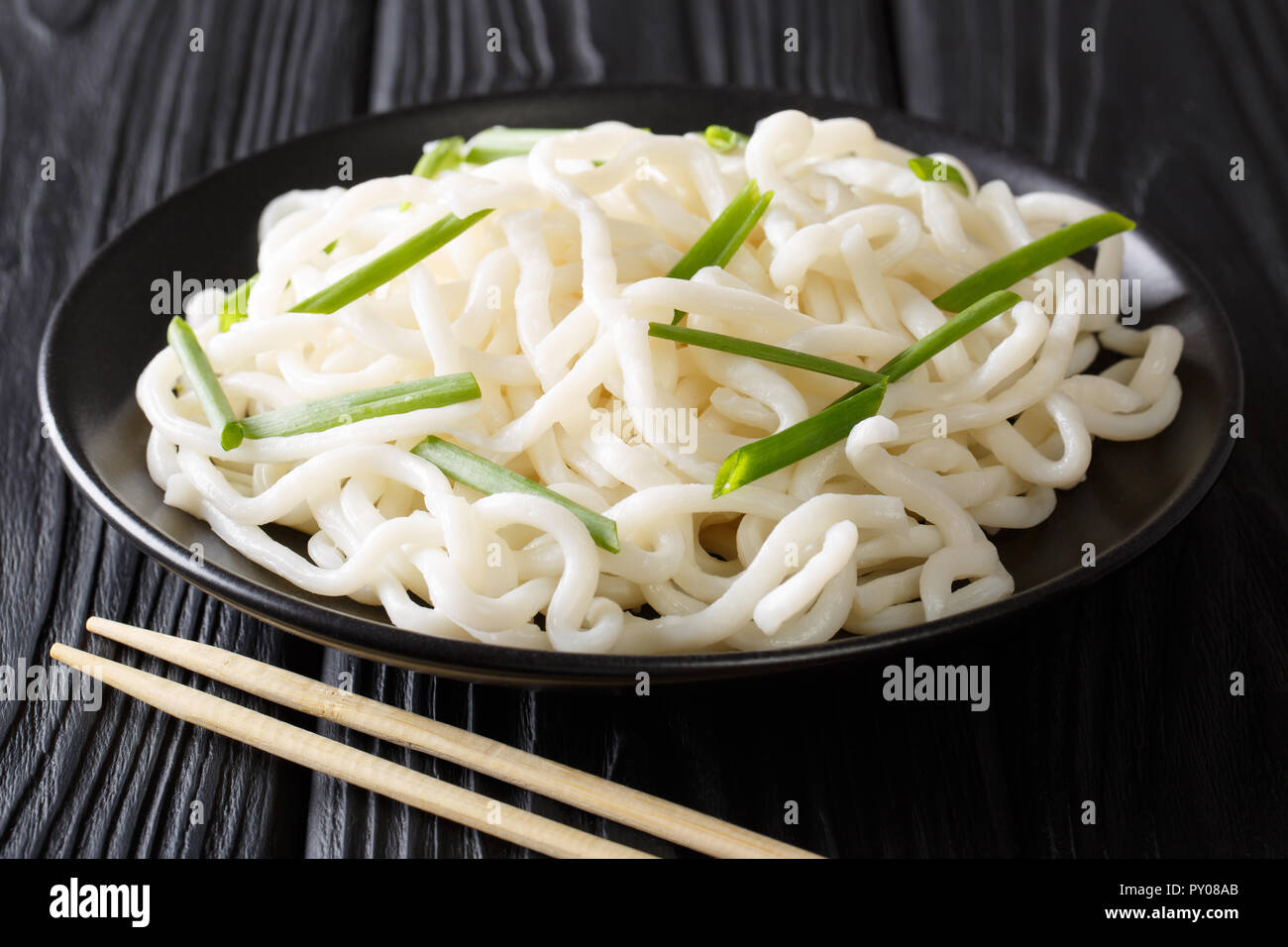 Servire udon tagliatelle con cipolle verdi close-up su una piastra su un tavoli in legno nero. orizzontale Foto Stock