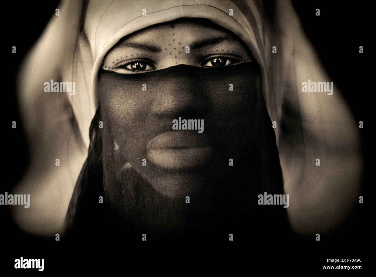 Ritratto di donna con la faccia decorata dietro trasparente velo nero su sfondo nero, Meknes, Marocco Foto Stock