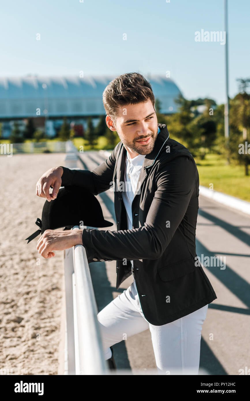 Bello equestre maschio appoggiata sul recinto con equitazione casco a cavallo club Foto Stock