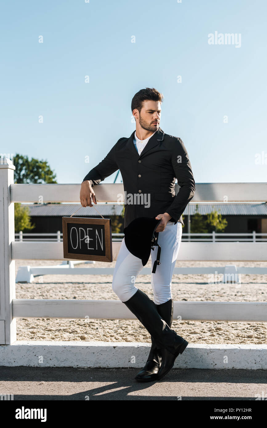 Bel maschio inclinazione equestre sulla recinzione e tenendo aperte segno a cavallo club Foto Stock
