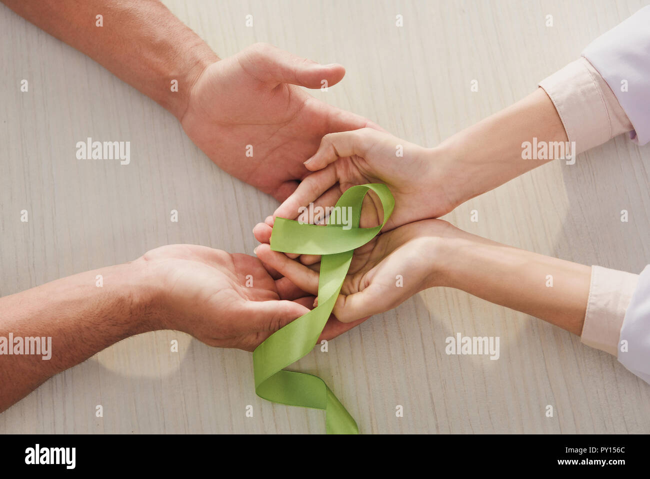 Vista parziale di maschio e femmina mani con nastro verde - si celebra la Giornata mondiale della salute mentale Foto Stock