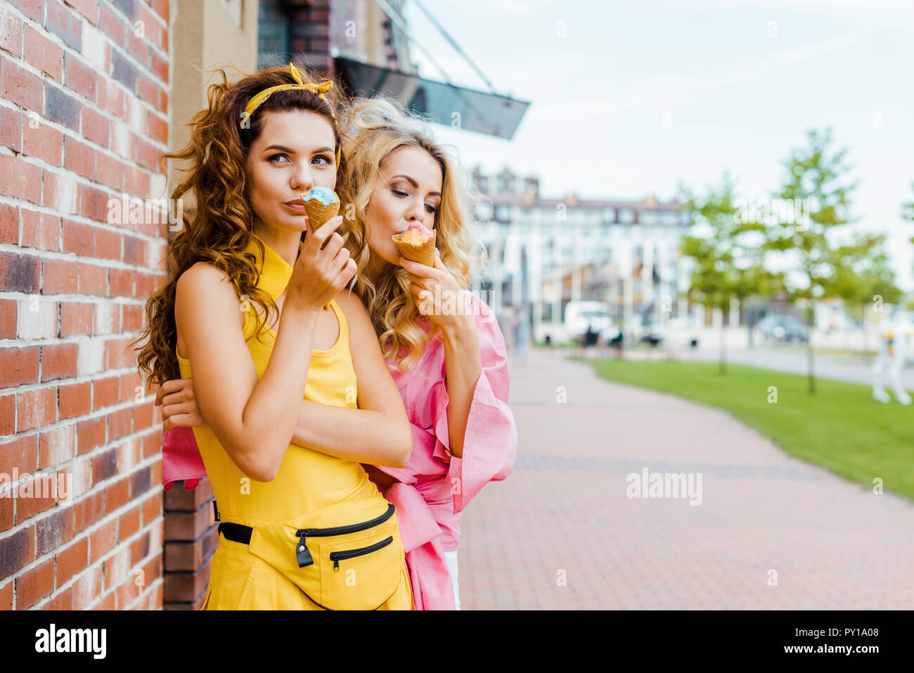 Elegante delle giovani donne in abiti colorati a mangiare il gelato in strada Foto Stock