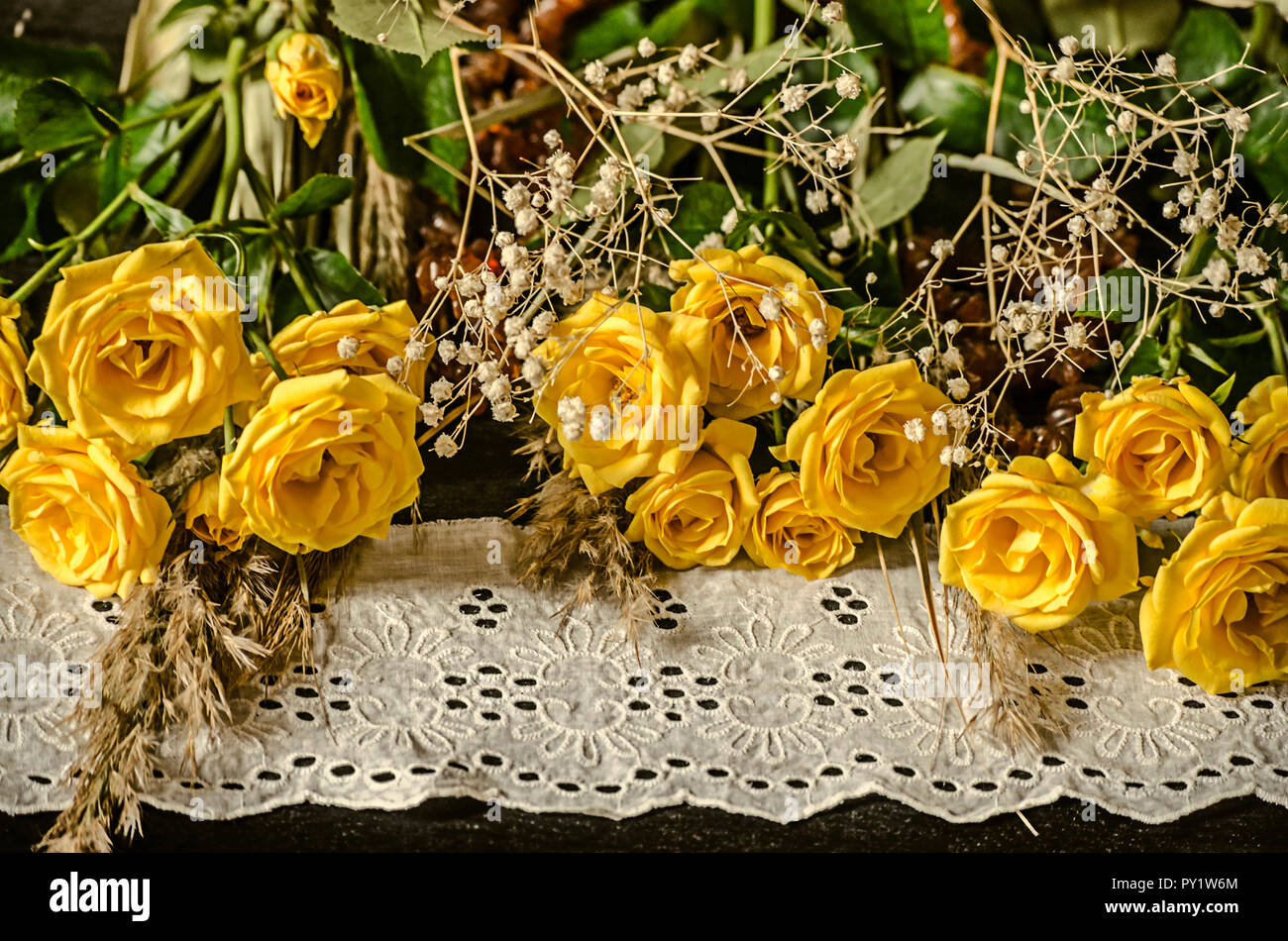 Legno compensato di nero con un bianco bordo ricamato giallo giacciono rose con ramoscelli secchi di bianco gypsophila e canne Foto Stock