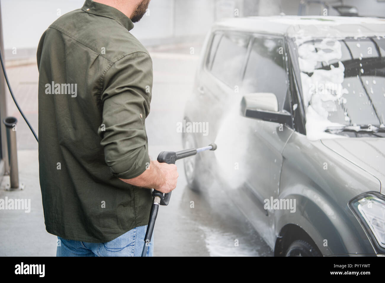 Immagine ritagliata dell uomo la pulizia auto da schiuma ad auto lavaggio con getto di acqua ad alta pressione Foto Stock