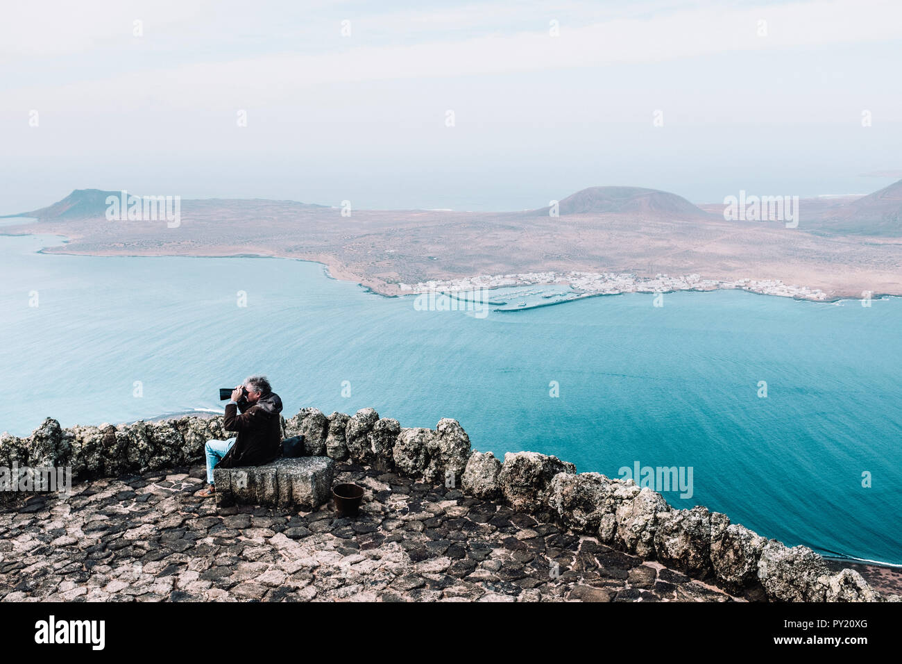 Uomo che guarda attraverso il binocolo al paesaggio con Isla de La Graciosa dal punto di vista presso il Mirador del Rio, Lanzarote, Isole Canarie, Spagna Foto Stock