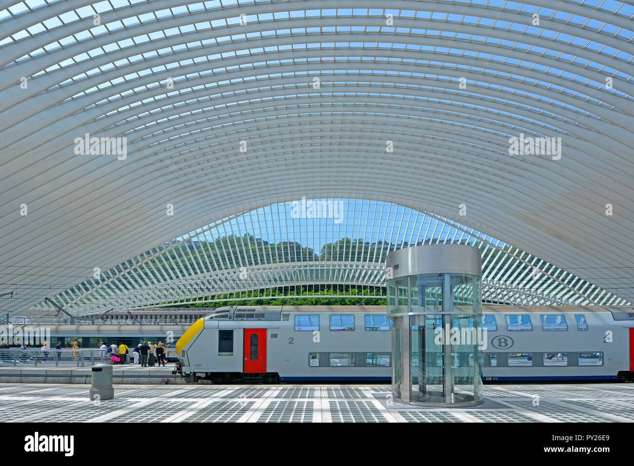 Enorme simmetrico tetto di vetro curve di costruzione su pubblica moderna struttura di trasporto Liege Belgio treno & carrelli di attendere alla stazione ferroviaria piattaforma UE Foto Stock