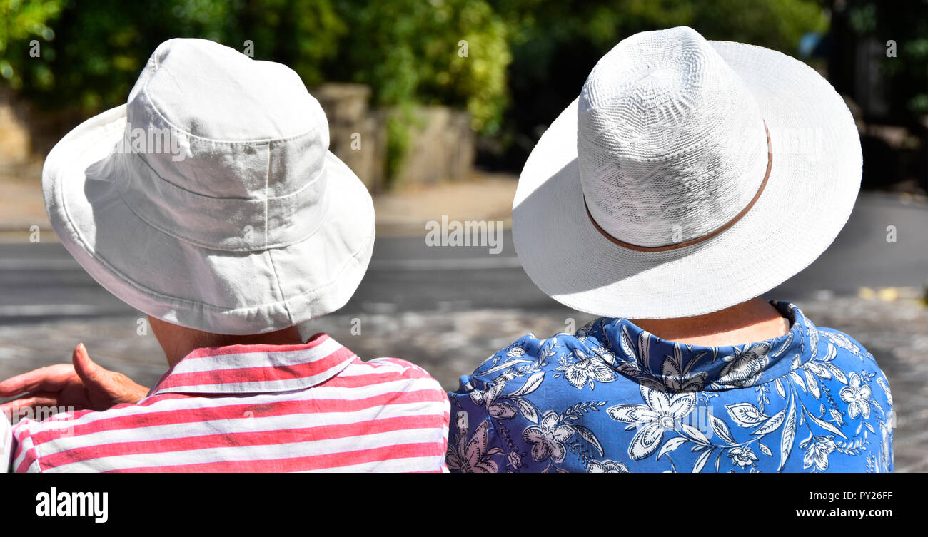 Due Senior donne mature sedersi a parlare alla fermata su molto caldo 2018 ondata di caldo giorno d'estate indossa cappello bianco nel sole di mezzogiorno Haworth West Yorkshire England Regno Unito Foto Stock