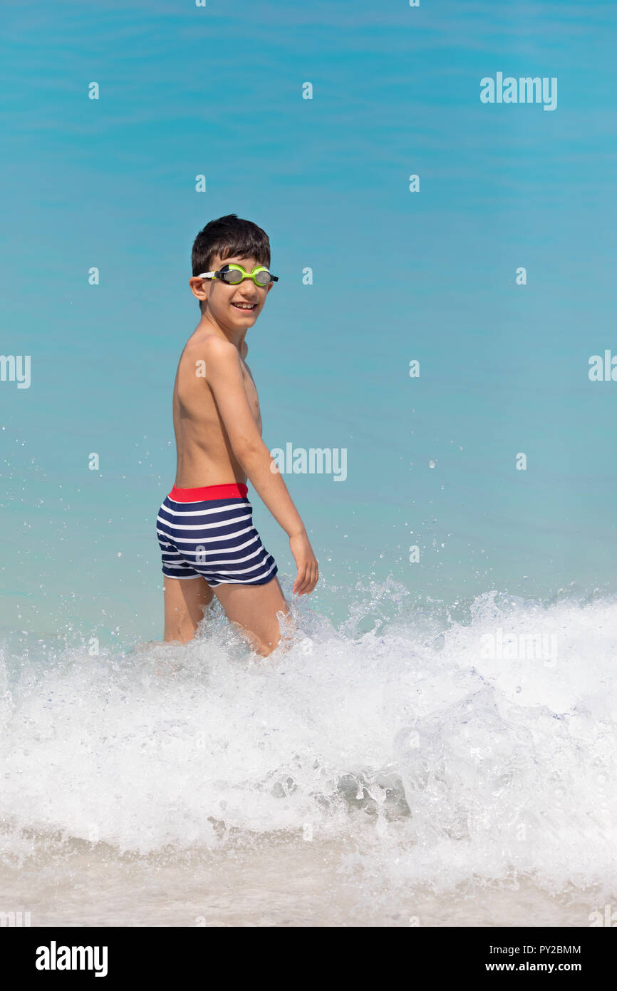 Sorridente ragazzo che indossa gli occhiali per nuoto in piedi in ocean surf, Grecia Foto Stock