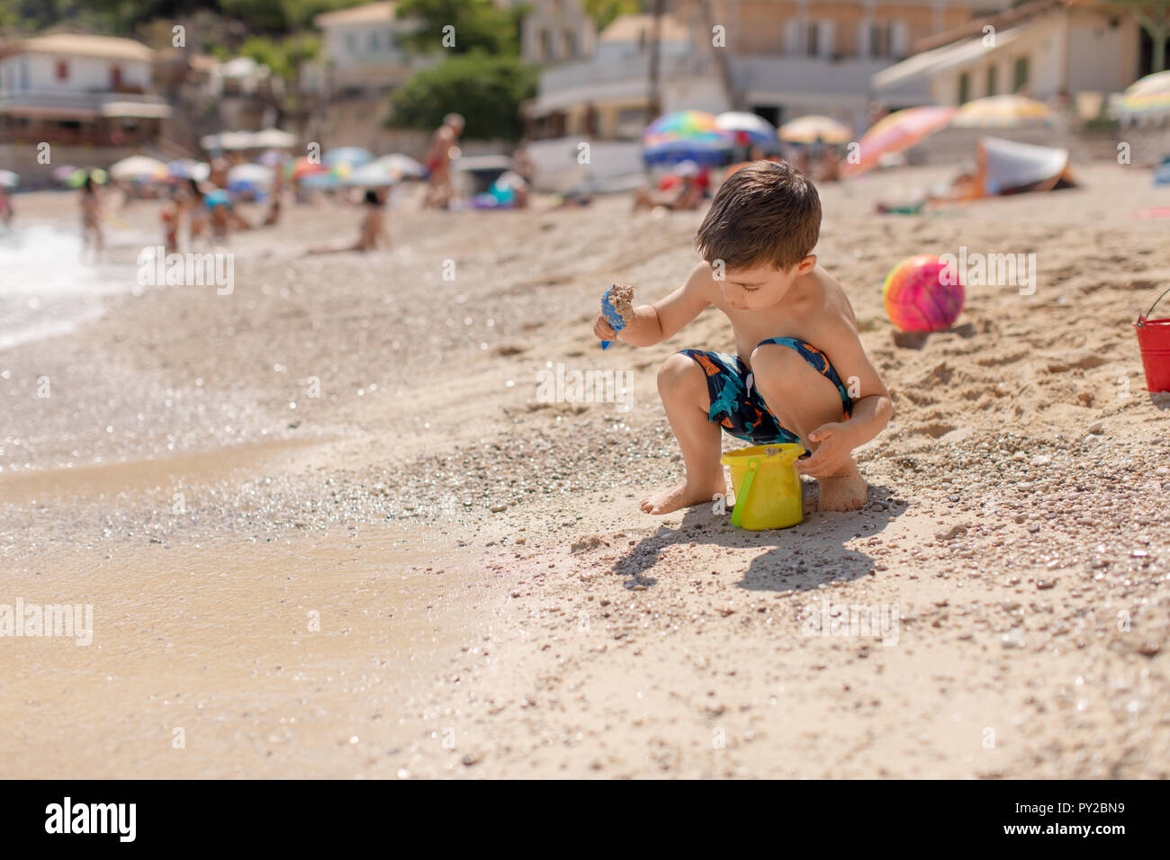 Ragazzo del riempimento di una benna con la sabbia sulla spiaggia, Grecia Foto Stock