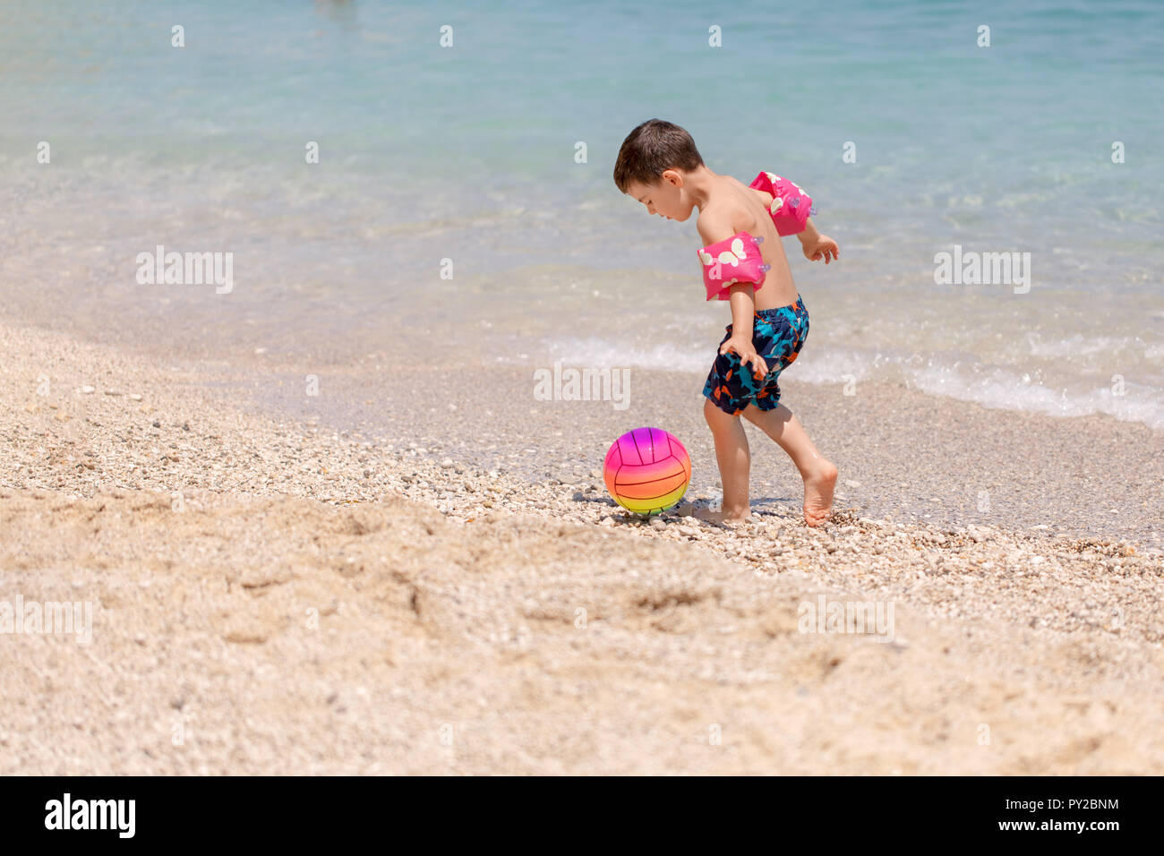 Ragazzo di calcio di un pallone sulla spiaggia, Grecia Foto Stock