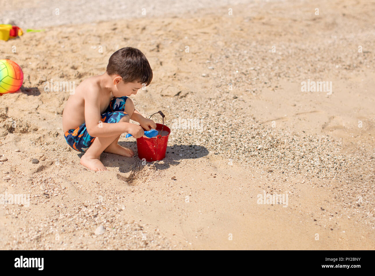 Ragazzo del riempimento di una benna con la sabbia sulla spiaggia, Grecia Foto Stock