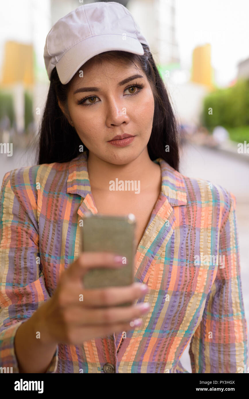 Donna asiatica pensare e utilizzando il telefono cellulare all'aperto Foto Stock