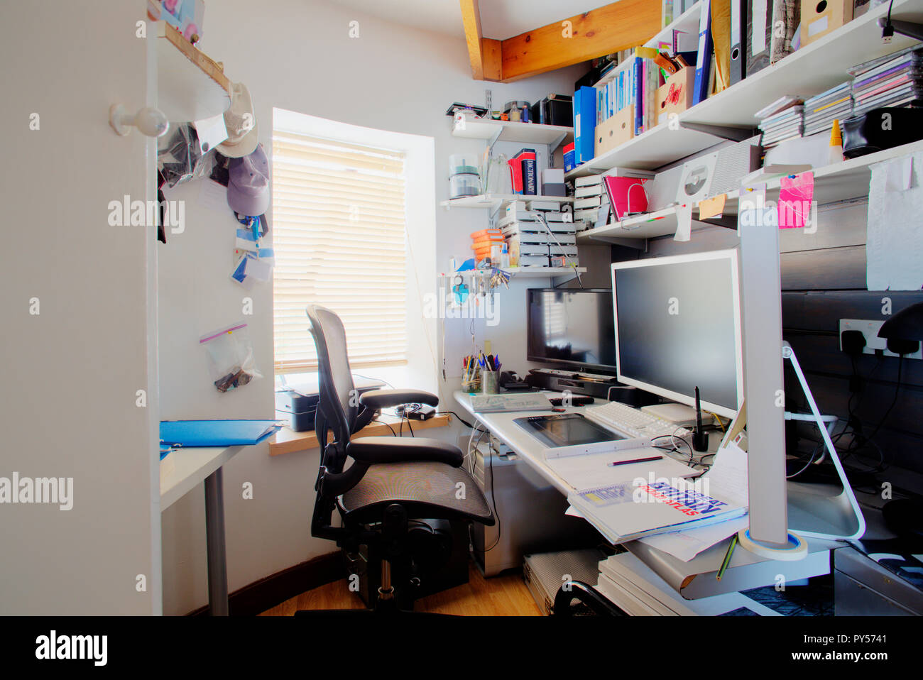 Un colpo di un confuso scrivania in un home office, la camera è piccola e confusa, sulla scrivania è di tre monitor per computer e forniture per ufficio. Foto Stock