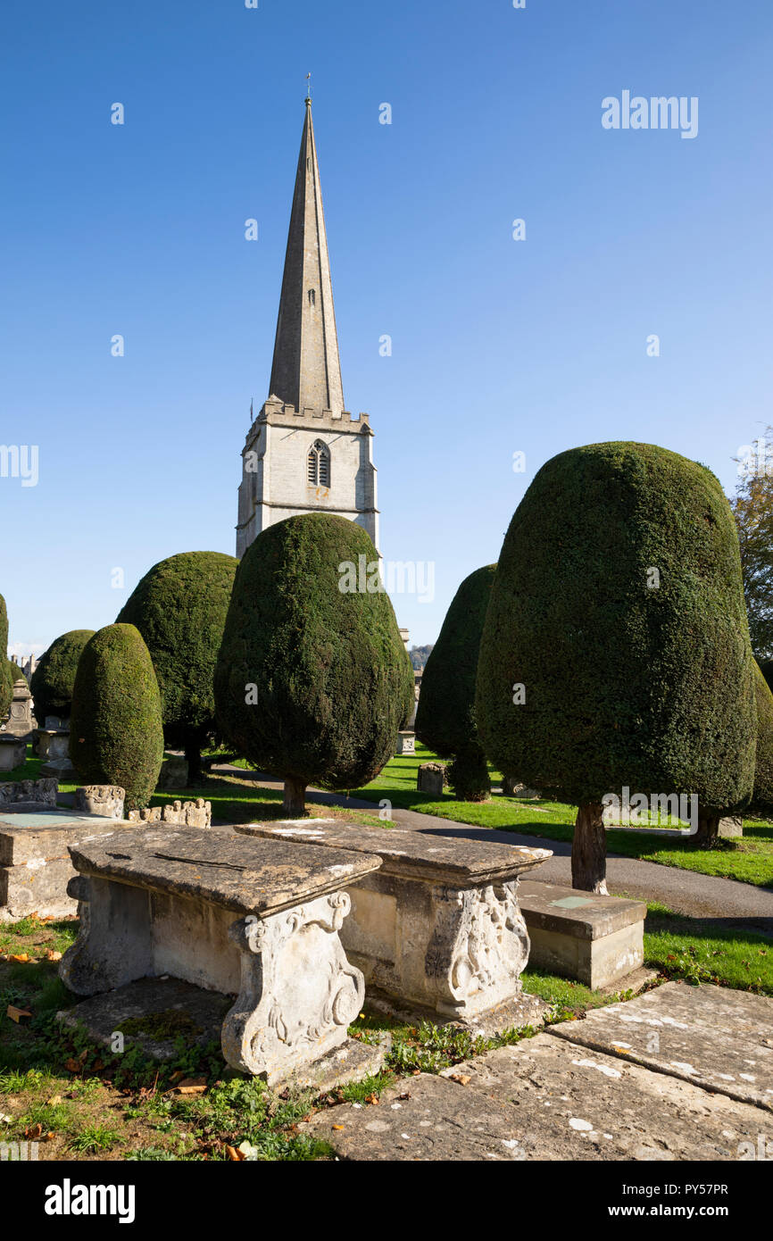 Santa Maria la chiesa parrocchiale con alberi di tasso e il torace tombe nel cimitero di pomeriggio di sole, Painswick, Cotswolds, Gloucestershire, England, Regno Unito Foto Stock