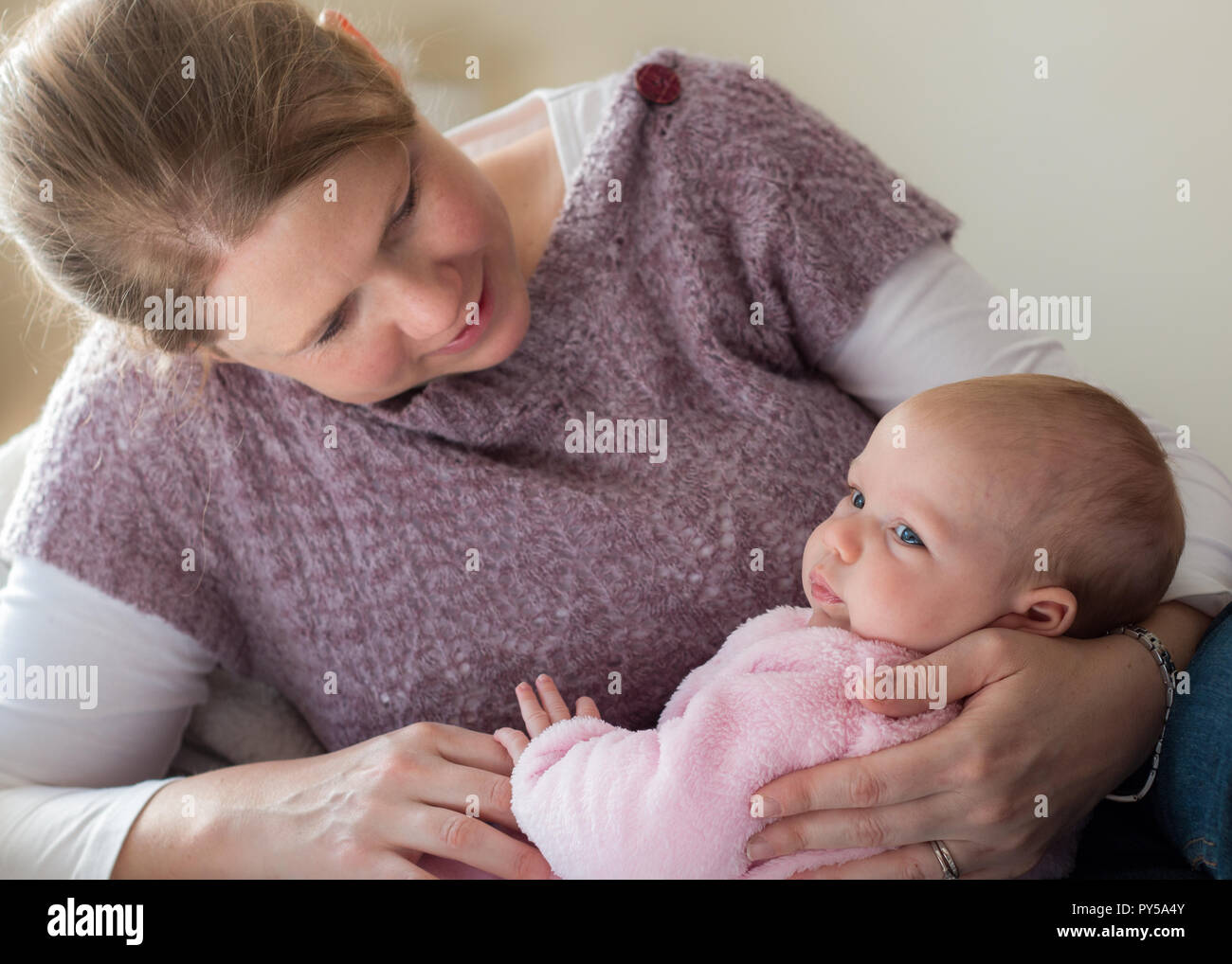 Madre tenendo la sua piccola bambina guardando il bambino e interagenti, seduta sul letto casual close up. Foto Stock