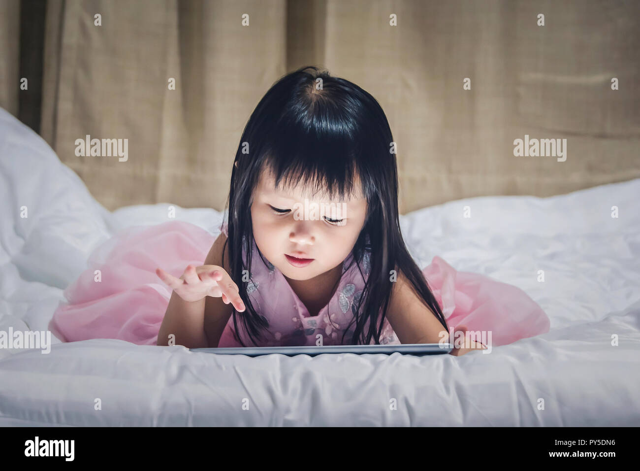 Bambina giacente tablet sul letto di notte utilizzando internet guardando vdo o gamp giocare i bambini smartphone o tablet concetto di tossicodipendenza. Foto Stock