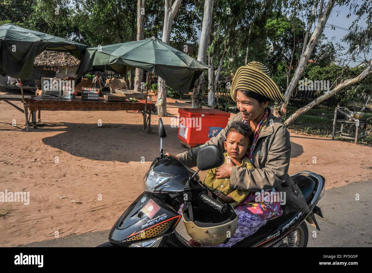 LAOS. Felice giovane madre in sella a una moto con il suo piccolo figlio sul giro su una strada di campagna in Laos Foto Stock