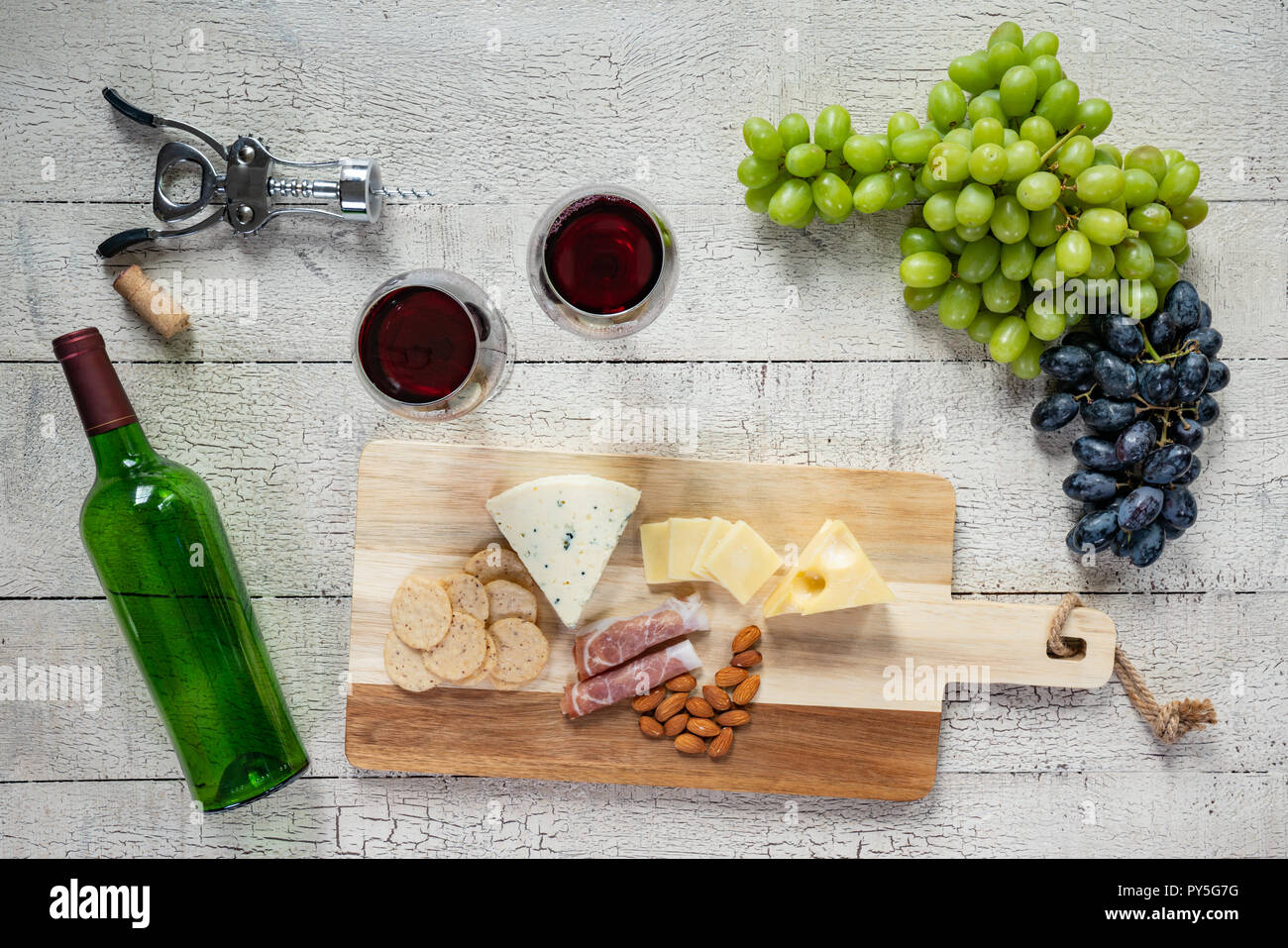 Bicchiere di vino rosso con bottiglia di vino, formaggio, cracker, prosciutto, mandorle e uva Foto Stock
