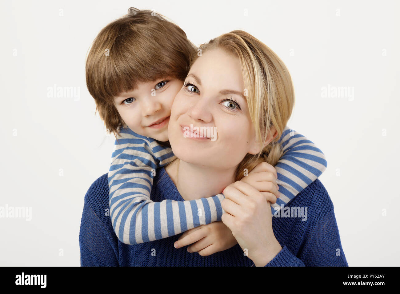 Un sorridente ragazzino e sua madre abbraccia sullo sfondo bianco. Concetto di amore e famiglia. Foto Stock