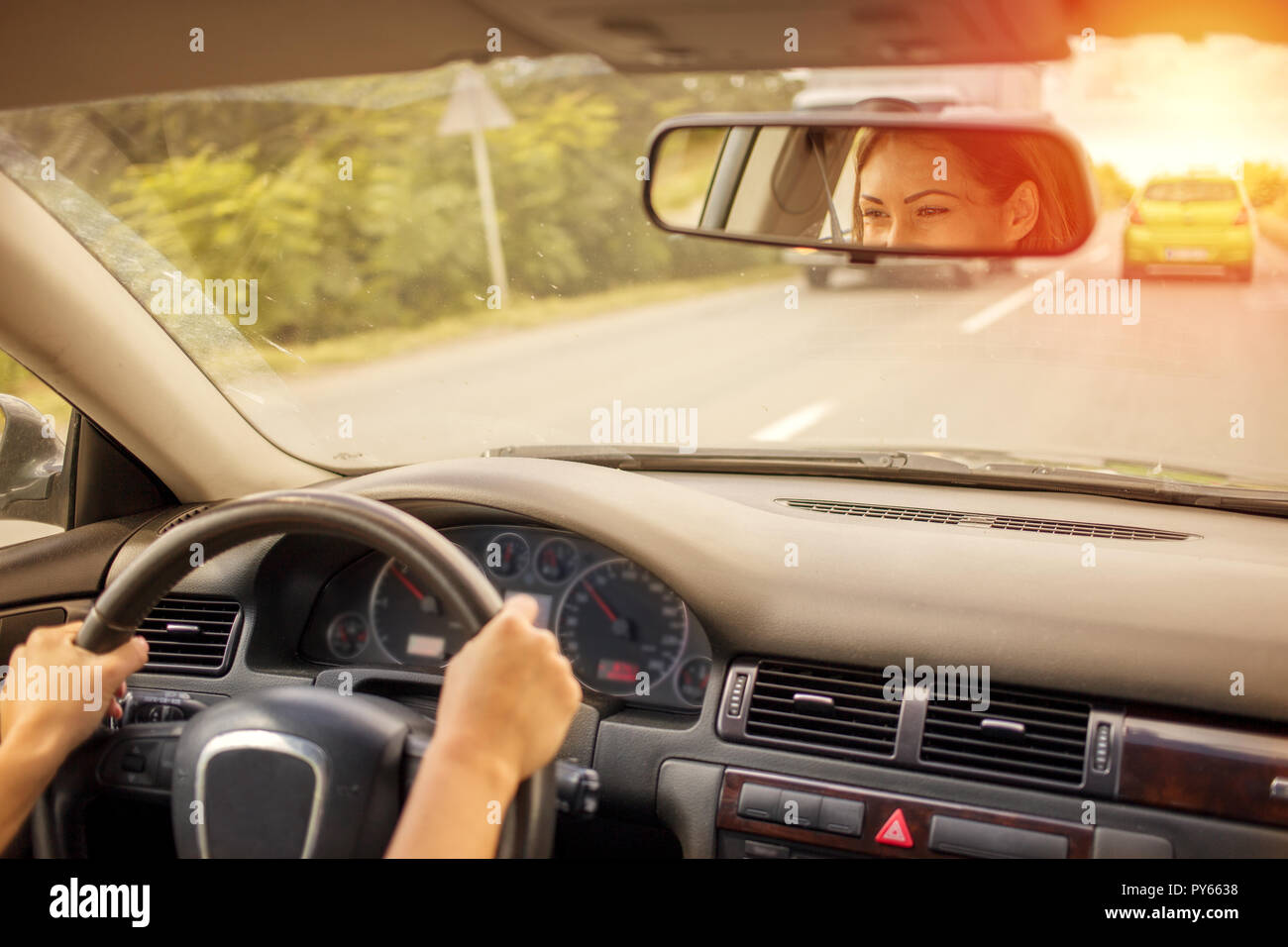 Bella giovane donna alla guida di una vettura sulla strada di fronte alla parte posteriore dello specchietto retrovisore Foto Stock