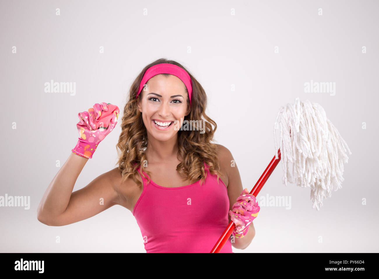 Donna su sfondo bianco tenendo una spugna e un mop mentre guardando la telecamera Foto Stock