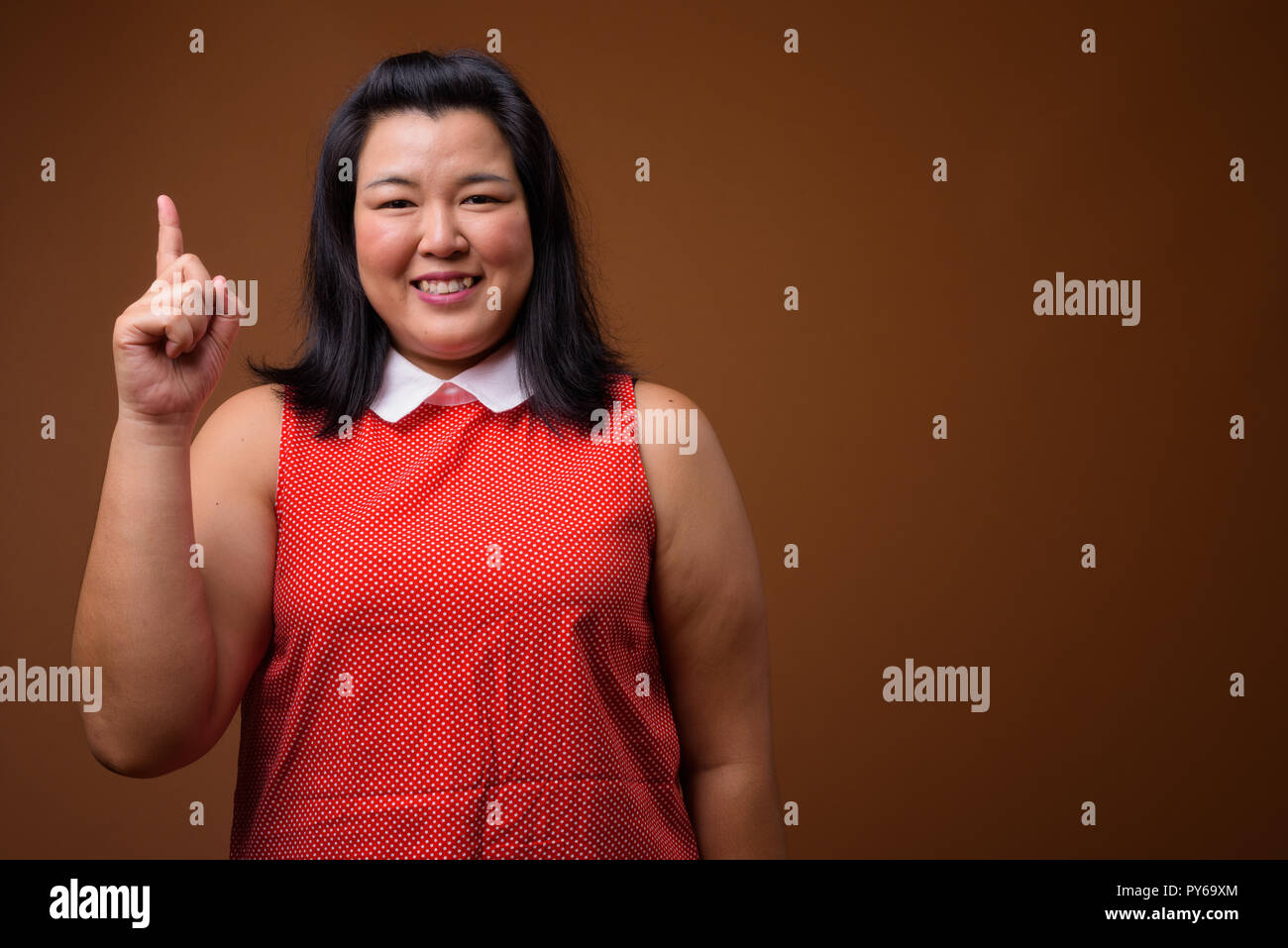 Felice sovrappeso donna asiatica puntare il dito fino mentre sorridente Foto Stock