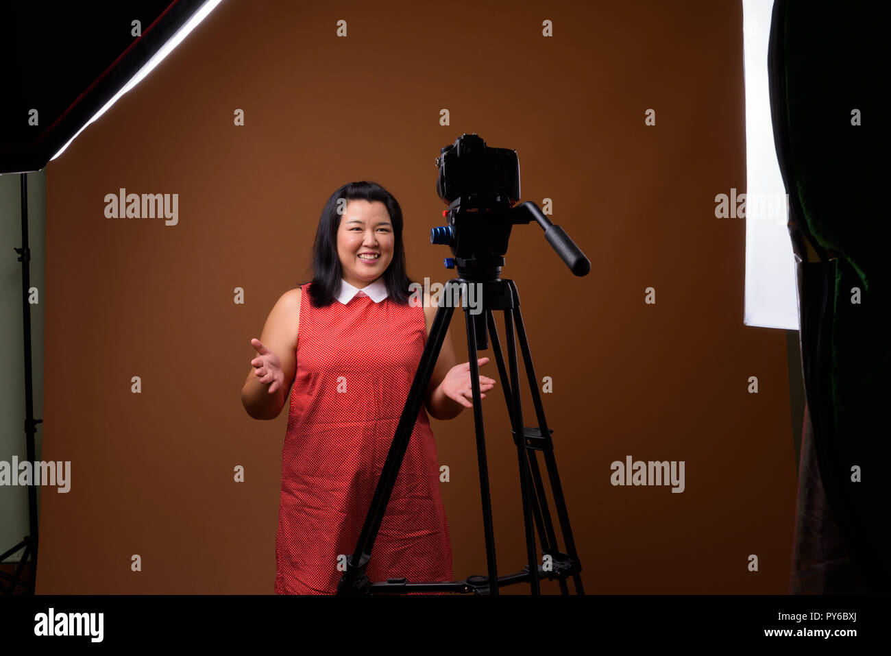 Il sovrappeso donna asiatica vlogging in studio con fotocamera reflex su treppiede Foto Stock