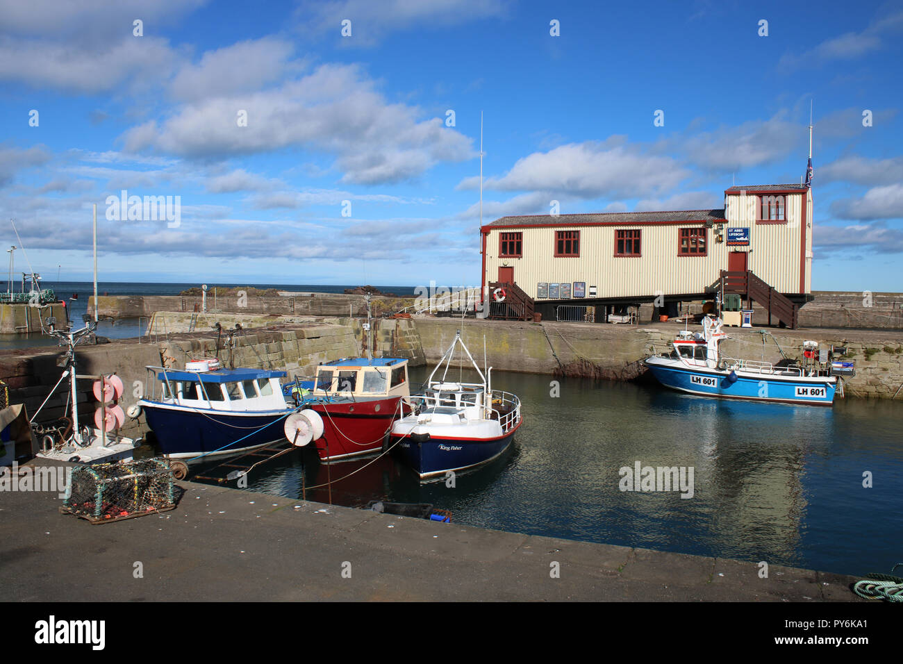 Vista di piccole imbarcazioni in St Abbs Harbour, St Abbs, Berwickshire, Scozia con la scialuppa di salvataggio indipendenti stazione sul molo centrale al di sopra delle barche. Foto Stock