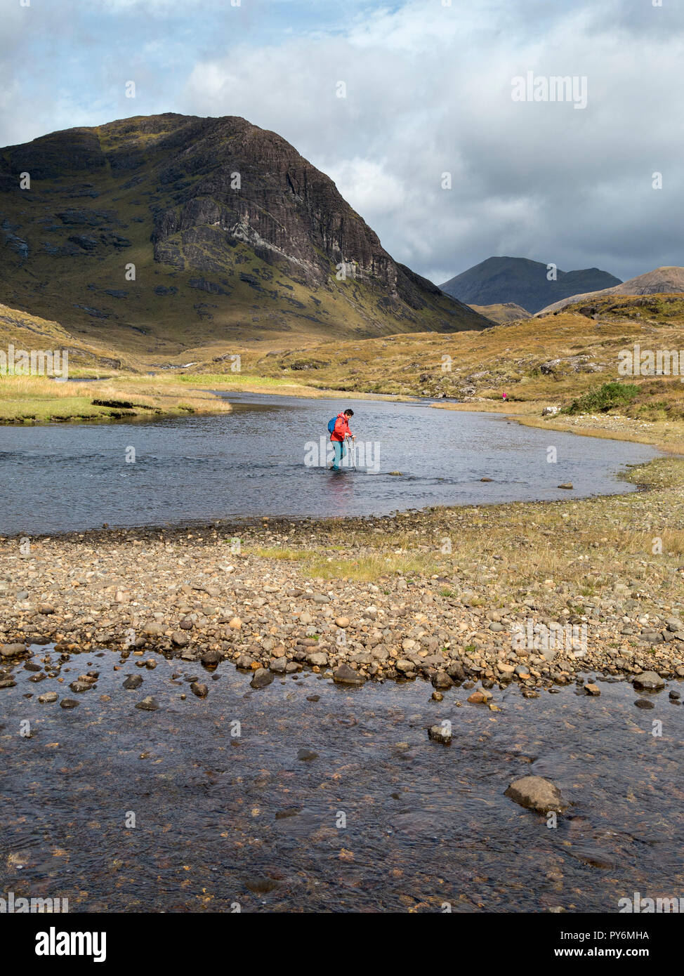 Femmina Lone walker tornando da Loch Coruisk crossing / guadare il fiume di Abhainn Camas Fhionnairigh a Camasunary Bay a Skye, Scotland, Regno Unito Foto Stock