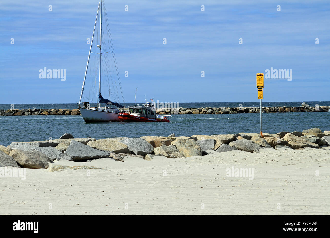 Una barca a vela disabili trainato da un TowBoat U.S. attraverso la marcatura del molo l'ingresso al porto Sesuit su Cape Cod in Oriente Dennis, Massachusetts Foto Stock