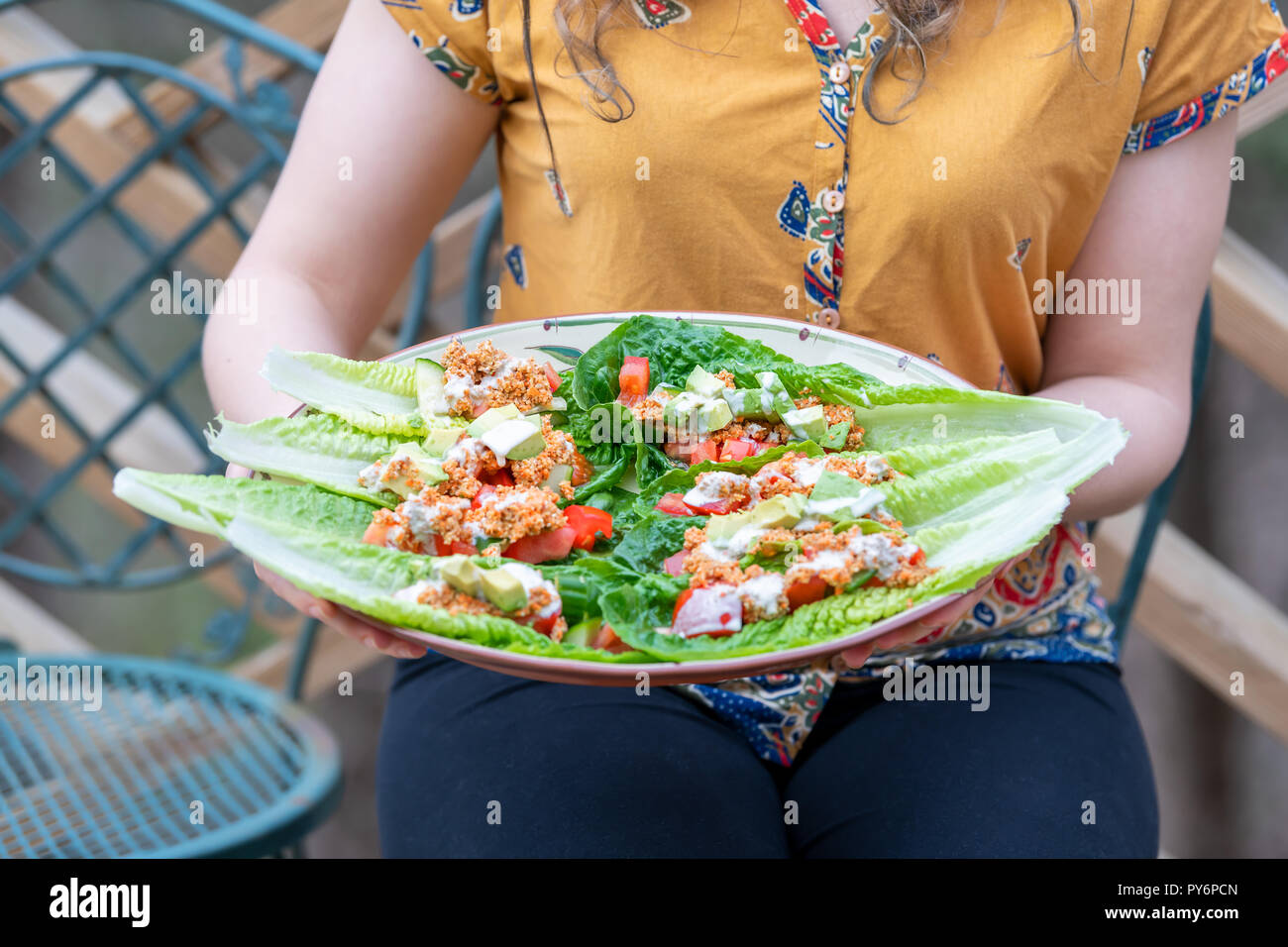 Primo piano della giovane donna seduta al di fuori, all'aperto, insalata di tenuta piastra fatta di foglie di lattuga, pomodori, cetrioli, avocado, dado in casa materie vegane mea Foto Stock