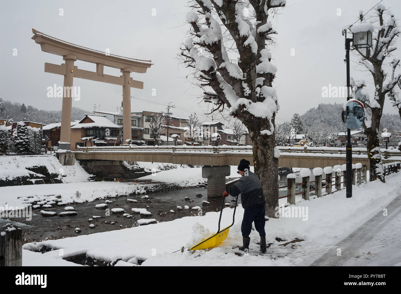 28.12.2017, Takayama, Gifu, Giappone, Asia - un uomo pale neve su una strada accanto alla Miyamae Bashi Bridge con il grande Torii gate ad un lato. Foto Stock