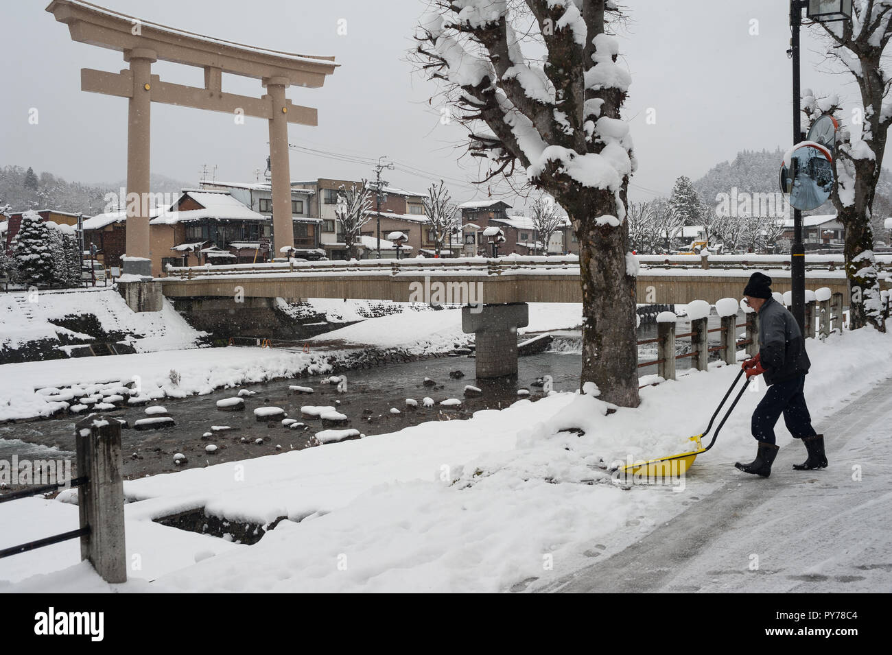 28.12.2017, Takayama, Gifu, Giappone, Asia - un uomo pale neve su una strada accanto alla Miyamae Bashi Bridge con il grande Torii gate ad un lato. Foto Stock