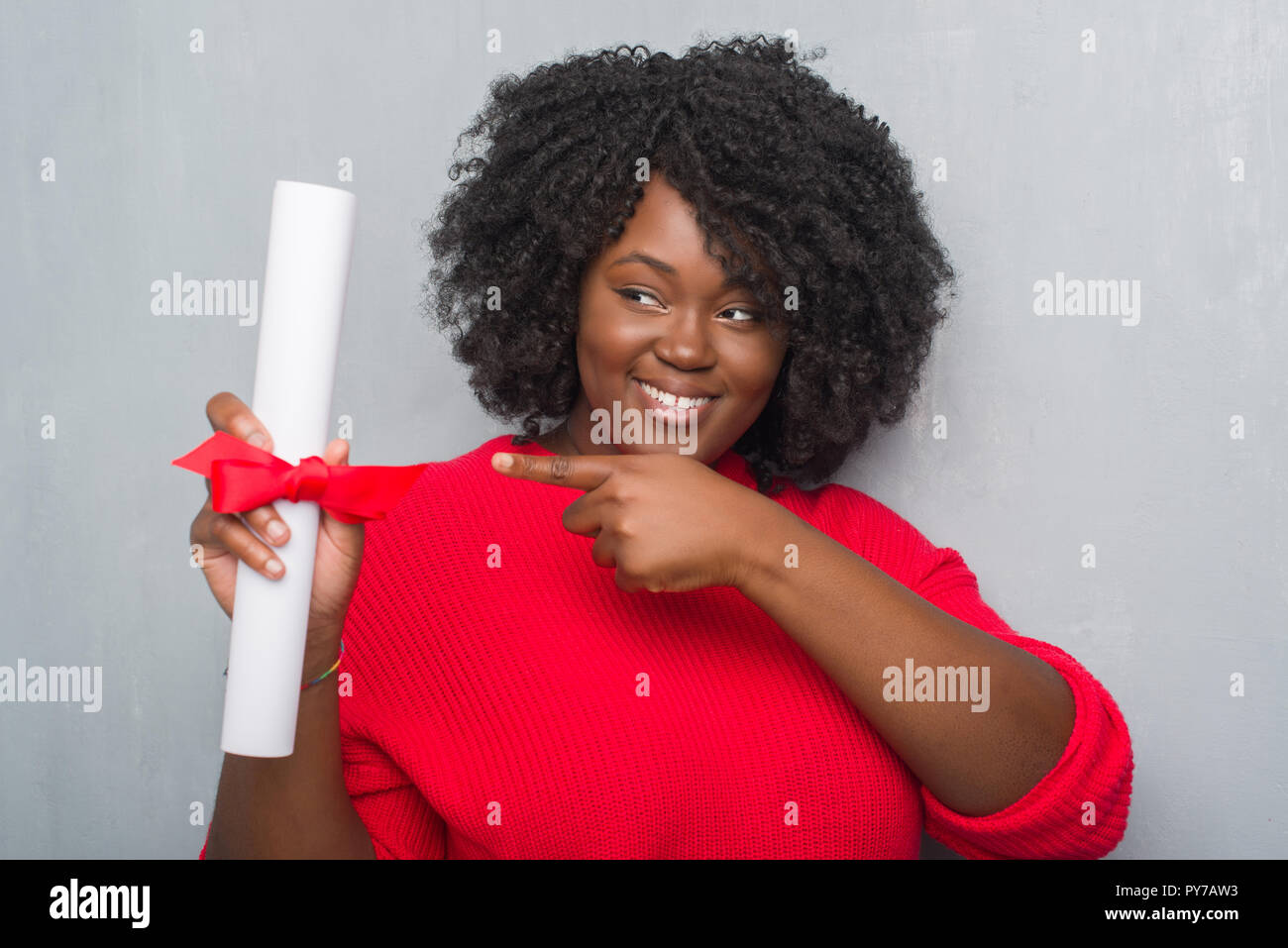 Giovane africano donna americana su grigio parete grunge diploma di contenimento molto felice puntando con mani e dita Foto Stock