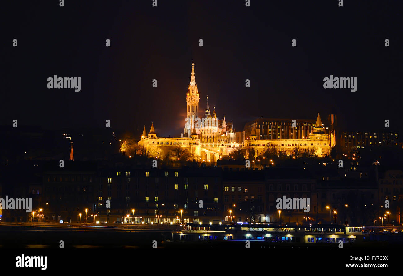 Vista sull'illuminato Bastione del Pescatore in una sera d'inverno, circondato da molti alleggerita di windows. Budapest. Foto Stock