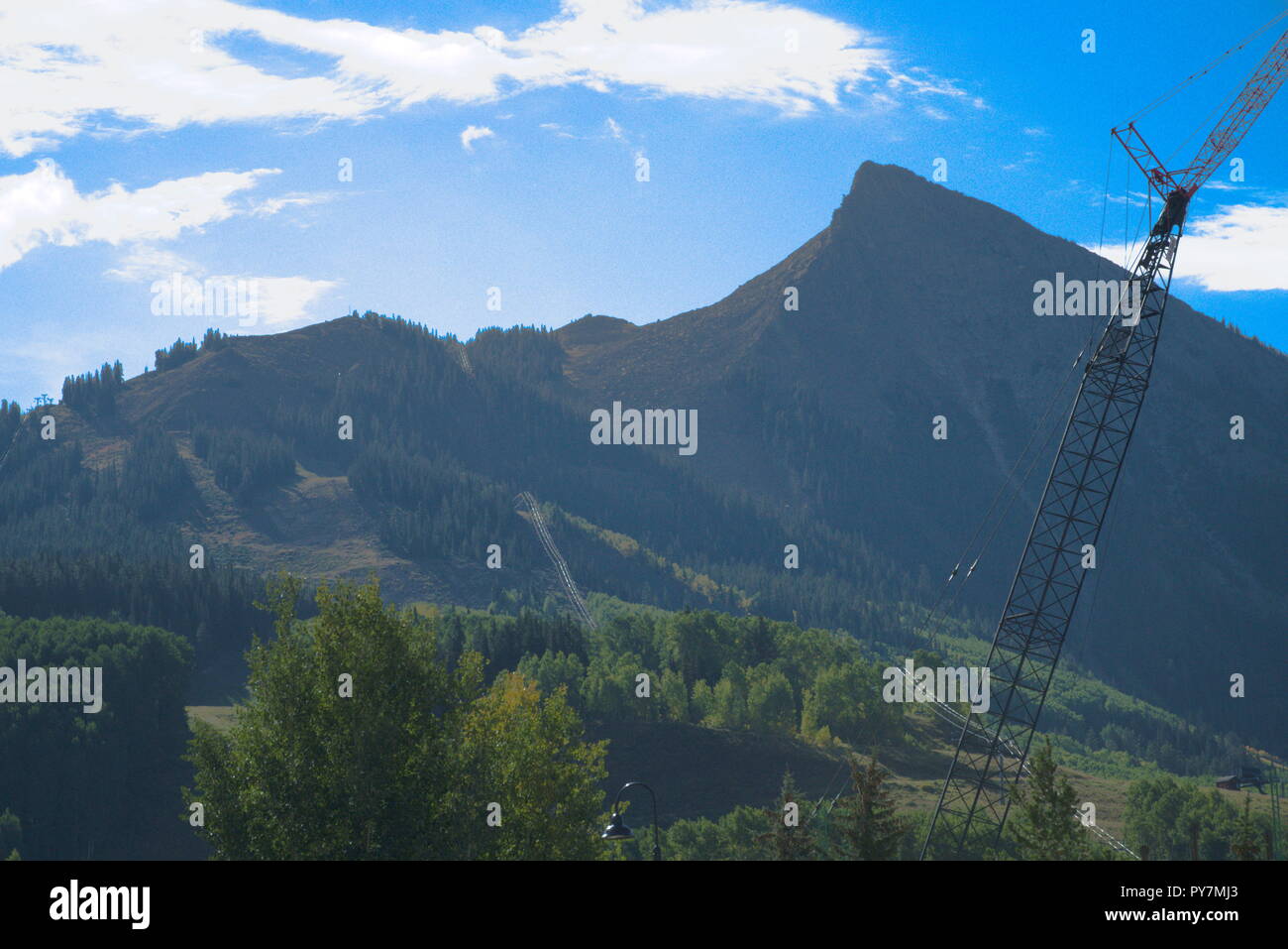 Crested Butte Mountain con una gru e alcuni alberi di fronte, con un cielo blu e nuvole bianche. Foto Stock