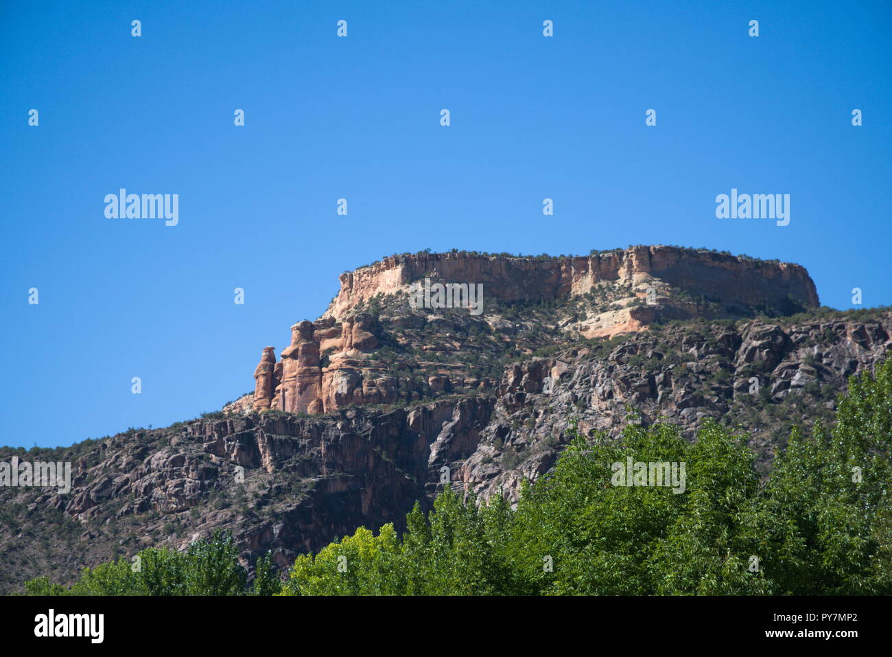 Il Colorado National Monument con granito cade e un chiaro cielo blu e verdi alberi di seguito. Foto Stock