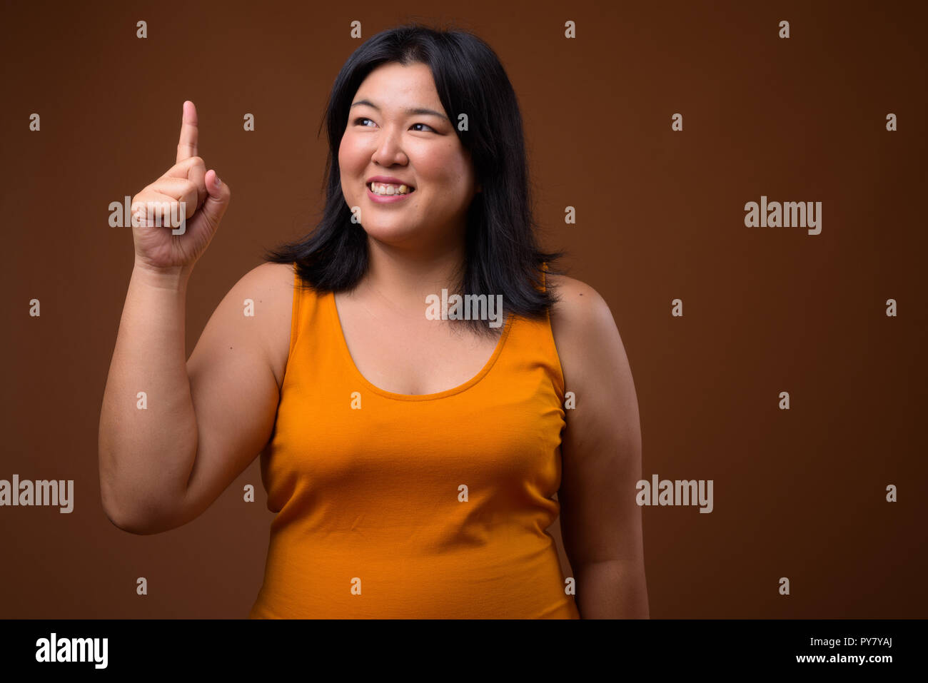 Felice sovrappeso donna asiatica puntare il dito verso l'alto mentre si pensa Foto Stock