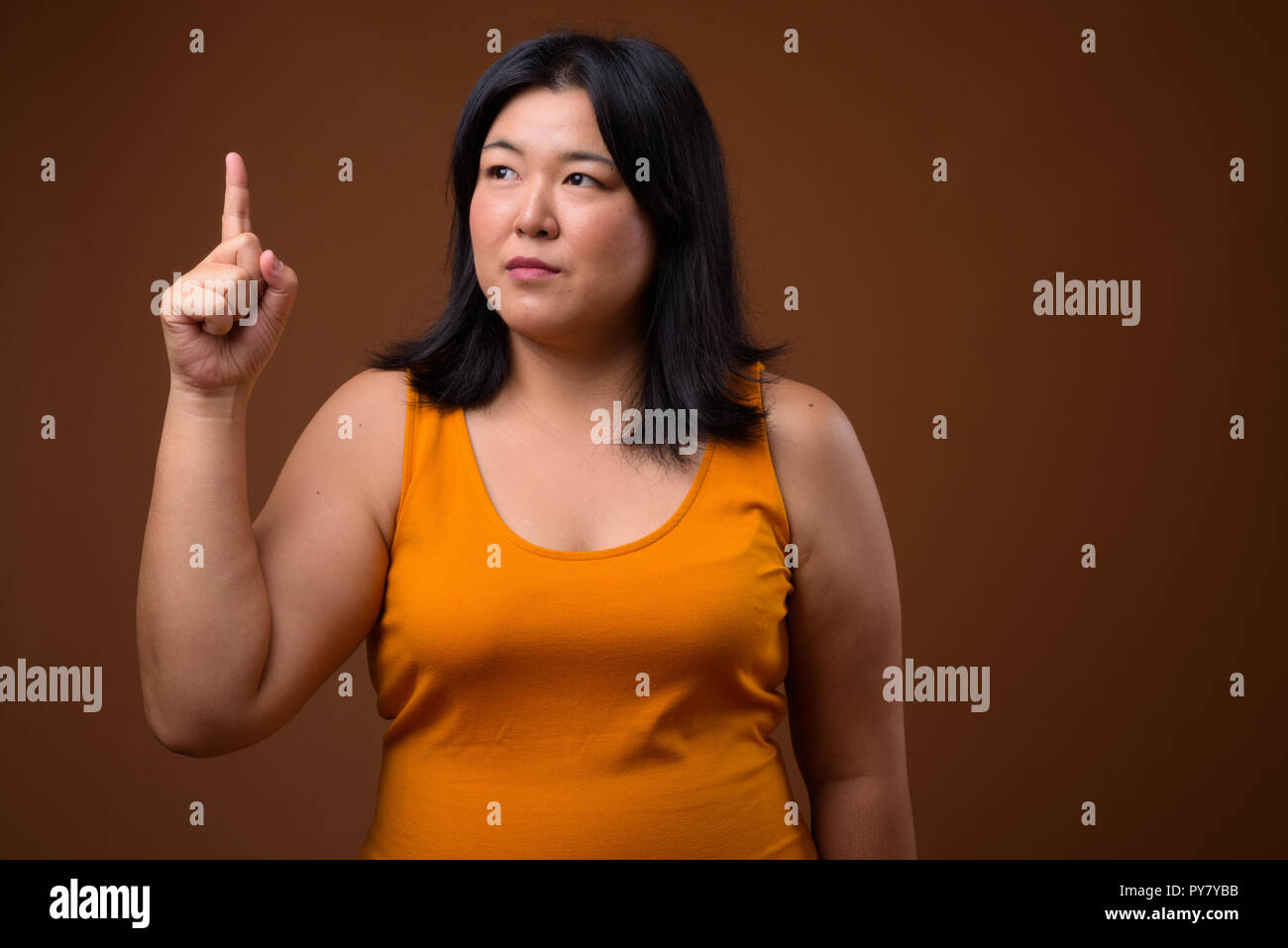 Bellissimo il sovrappeso donna asiatica puntare il dito verso l'alto mentre si pensa Foto Stock