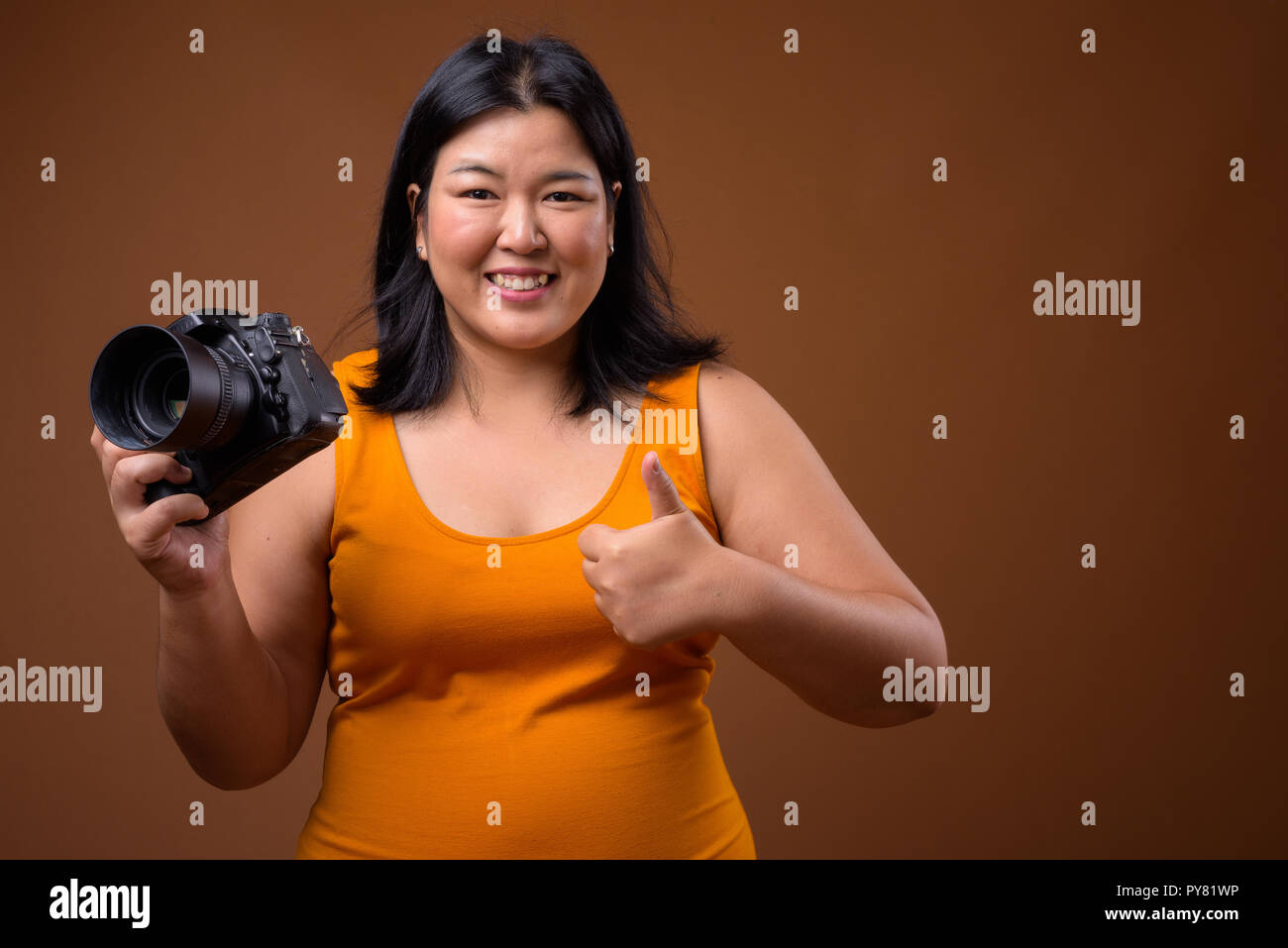 Bellissimo il sovrappeso donna asiatica fotografo sorridente e dando pollice in alto Foto Stock