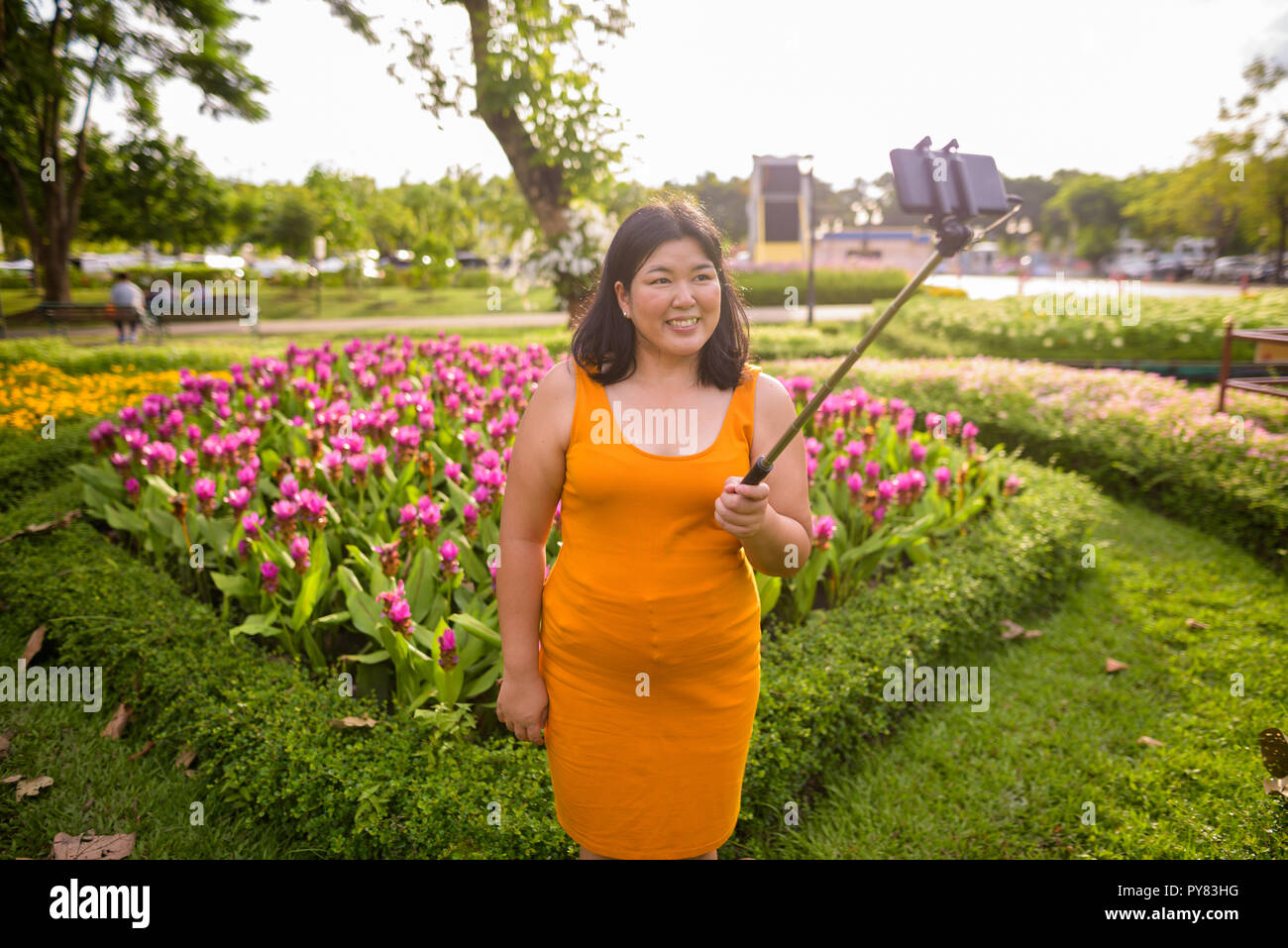 Donna asiatica tenendo selfie con telefono cellulare allega a selfie stick in posizione di parcheggio Foto Stock